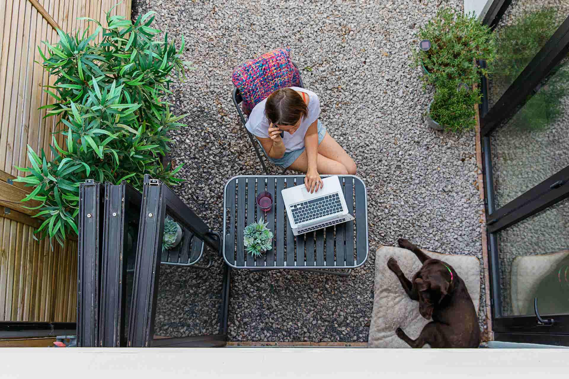 a woman in the garden with her dog, working on her laptop and talking on the phone 